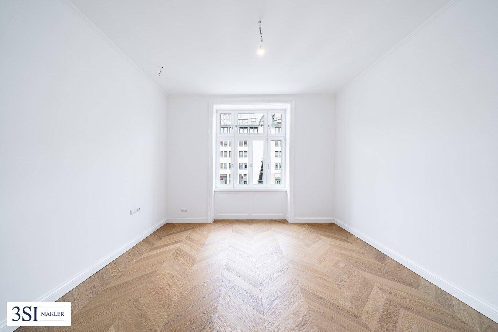 Geräumiges Schlafzimmer mit hellem Fischgrätparkett und einem großen Fenster.