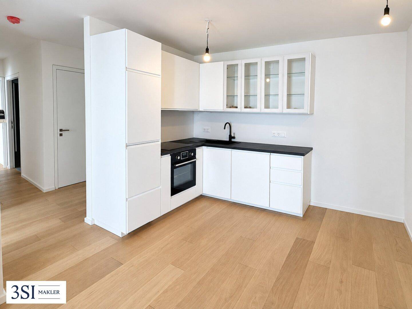 Moderne Einbauküche mit weißen Schränken, schwarzer Arbeitsplatte und integrierten Geräten.