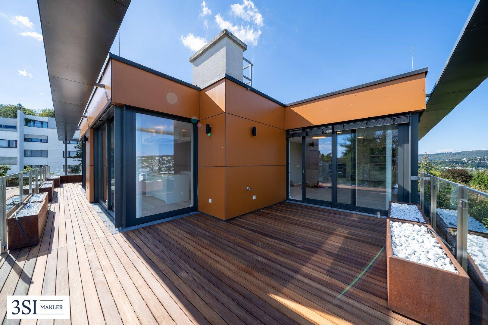 Großzügige Dachterrasse mit Holzboden, modernen Pflanzkübeln und Panoramablick.