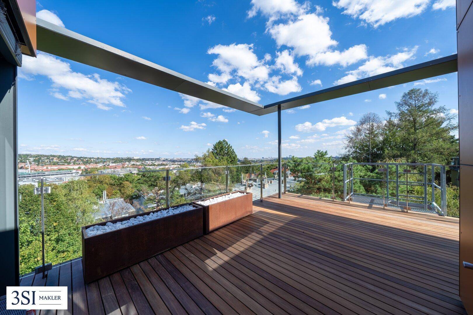 Sonniger Terrassenbereich mit Holzboden und weitem Blick über die Landschaft und die Stadt.