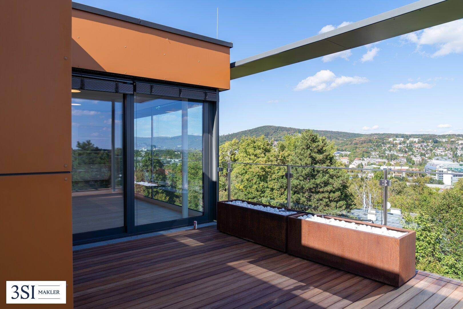 Geräumige Holzterrasse mit Glasgeländer und modernen Pflanzkübeln, umgeben von Natur.