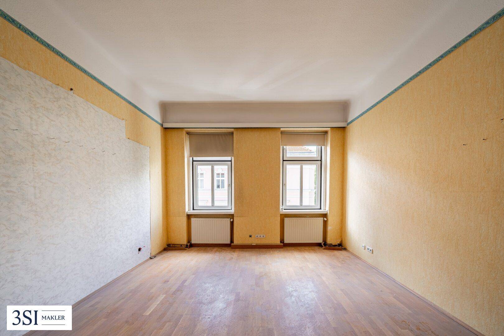 Heller Raum mit gelber Tapete, zwei Fenstern und Holzparkett, ideal für eine Neugestaltung.
