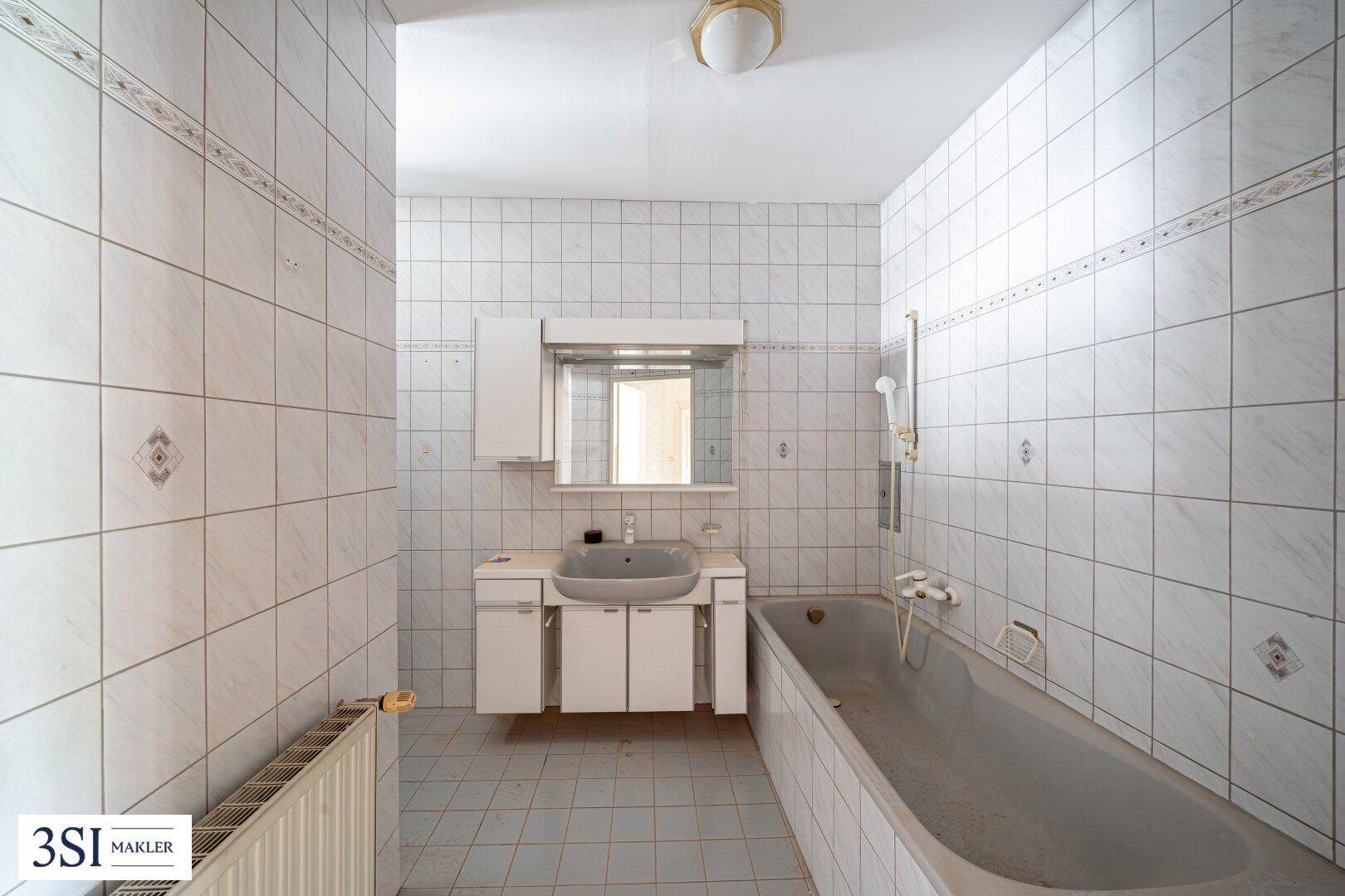 Gefliestes Badezimmer mit Badewanne, Waschbecken und Heizkörper, bereit zur Modernisierung.