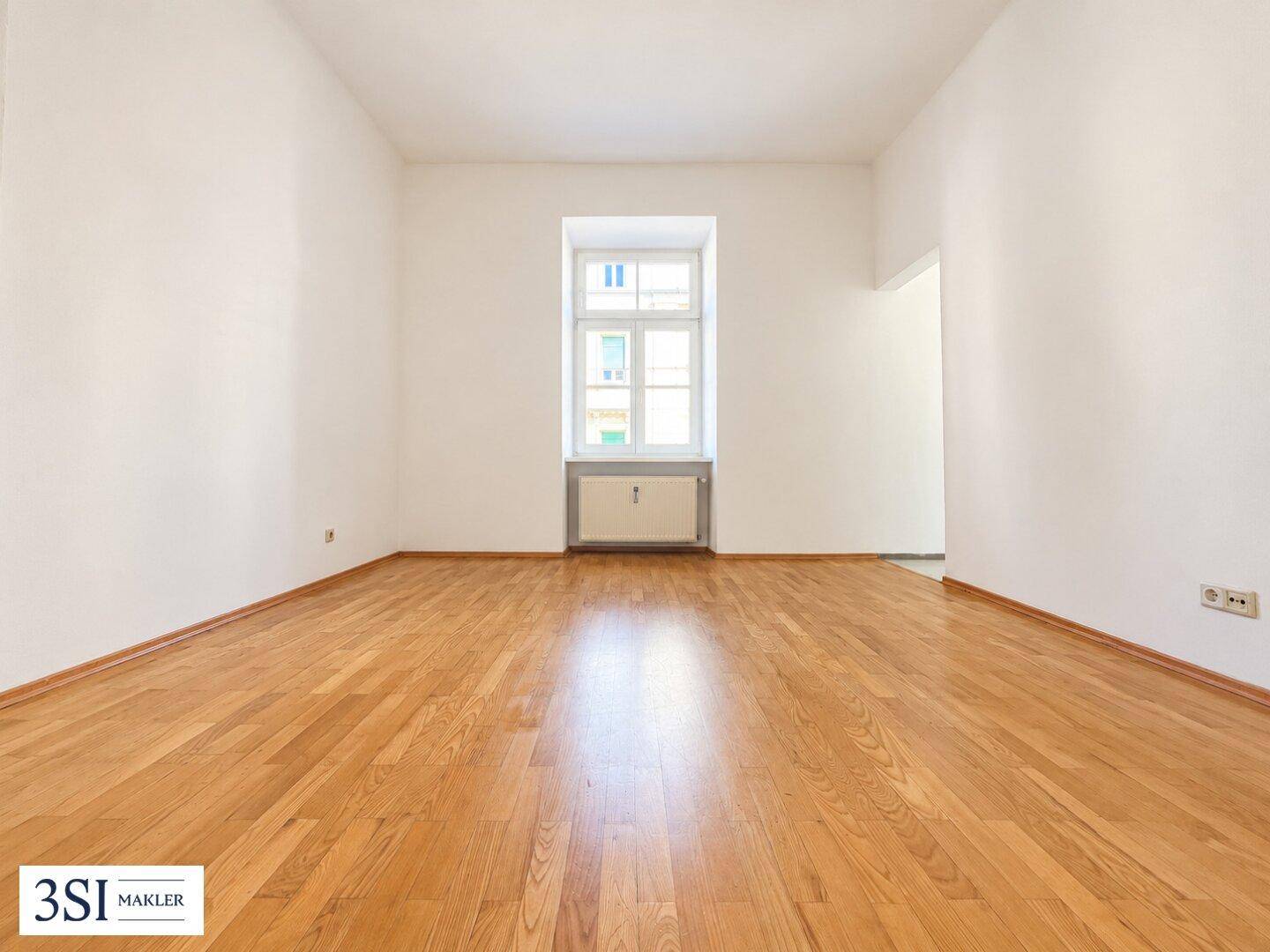 Geräumiges, helles Zimmer mit Holzboden und einem großen Fenster, ideal für Wohn- oder Schlafbereich.