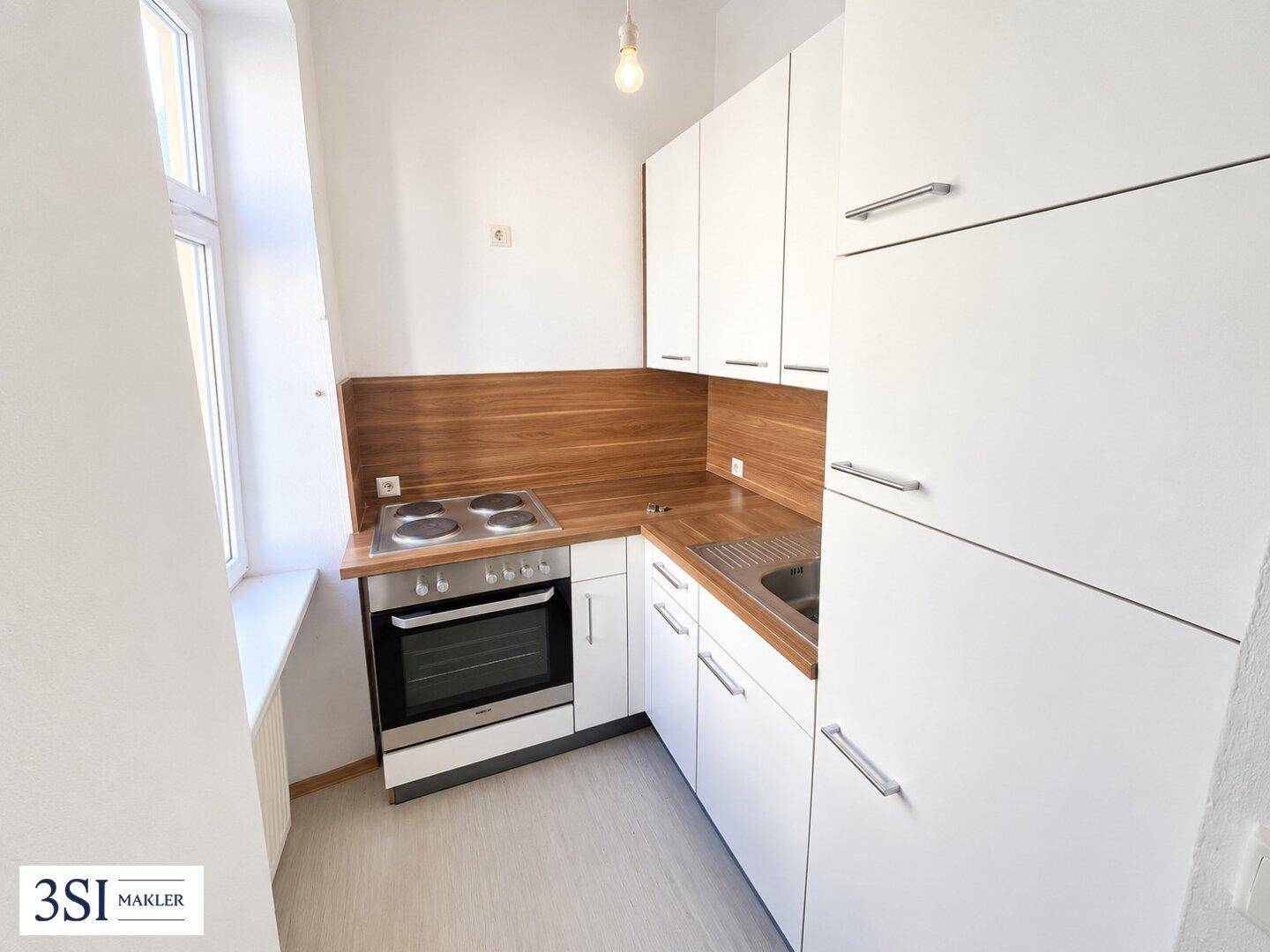 Funktionale kleine Küche mit weißen Schränken, Holzarbeitsplatte und integriertem Herd mit Backofen.