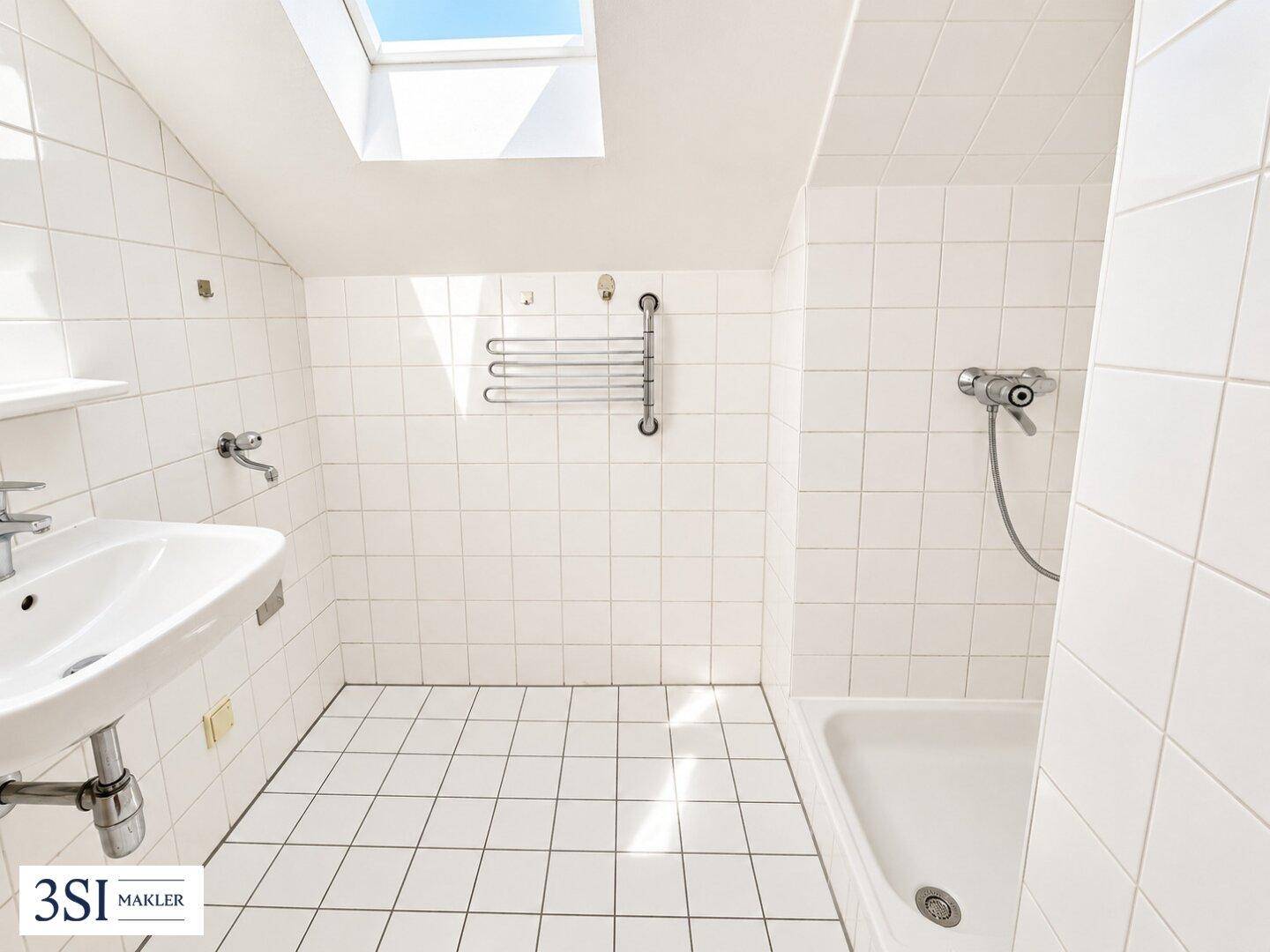 Weiß gefliestes Badezimmer im Dachgeschoss mit Badewanne, Waschbecken und Dachfenster.