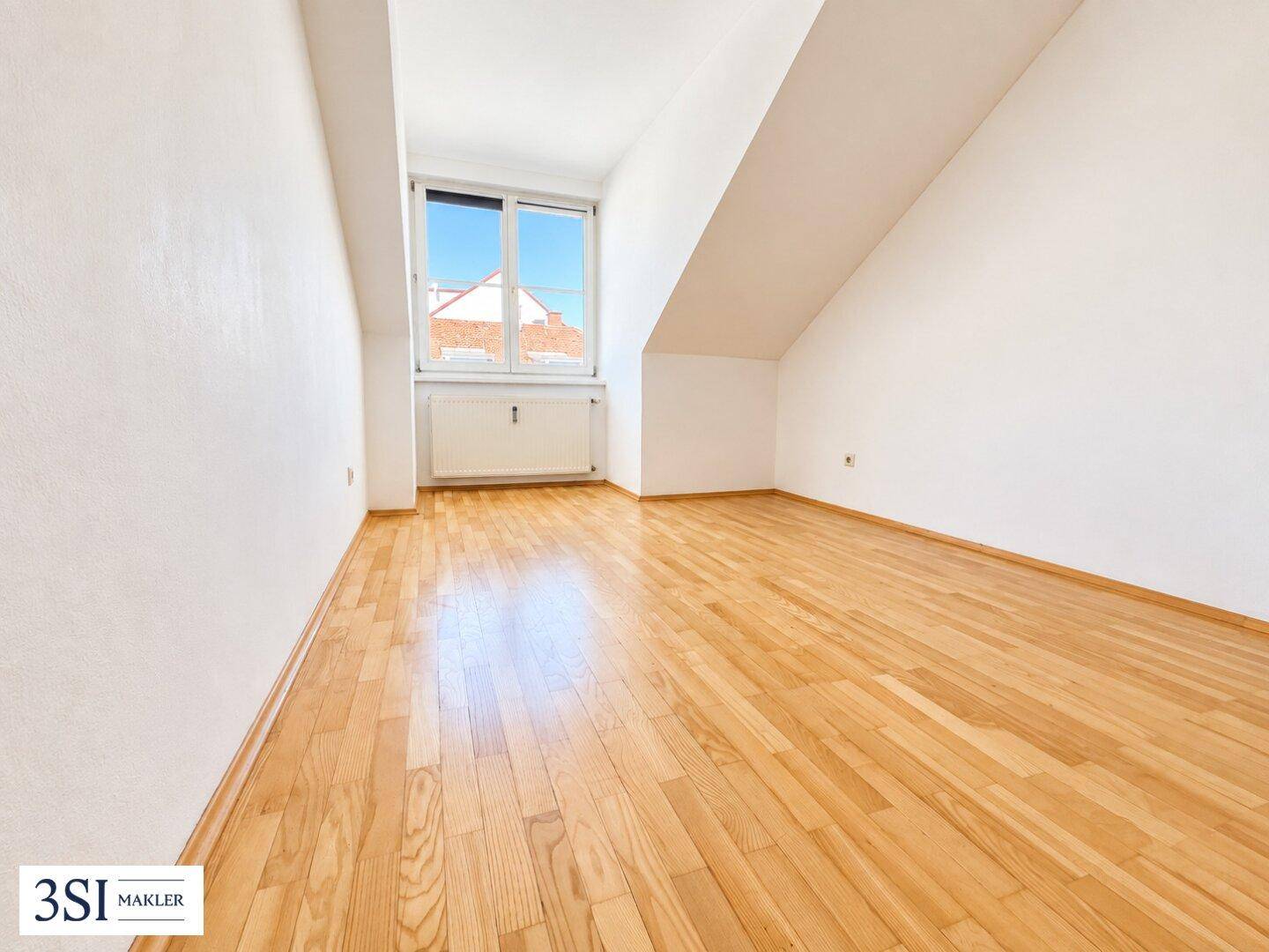 Helles Dachzimmer mit Holzboden, weiß gestrichenen Wänden und einem großen Fenster.