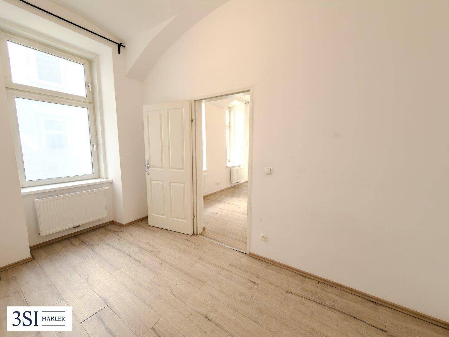 Helles Zimmer mit zwei großen Fenstern, Laminatboden und weiß gestrichenen Wänden, bietet viel Tageslicht.