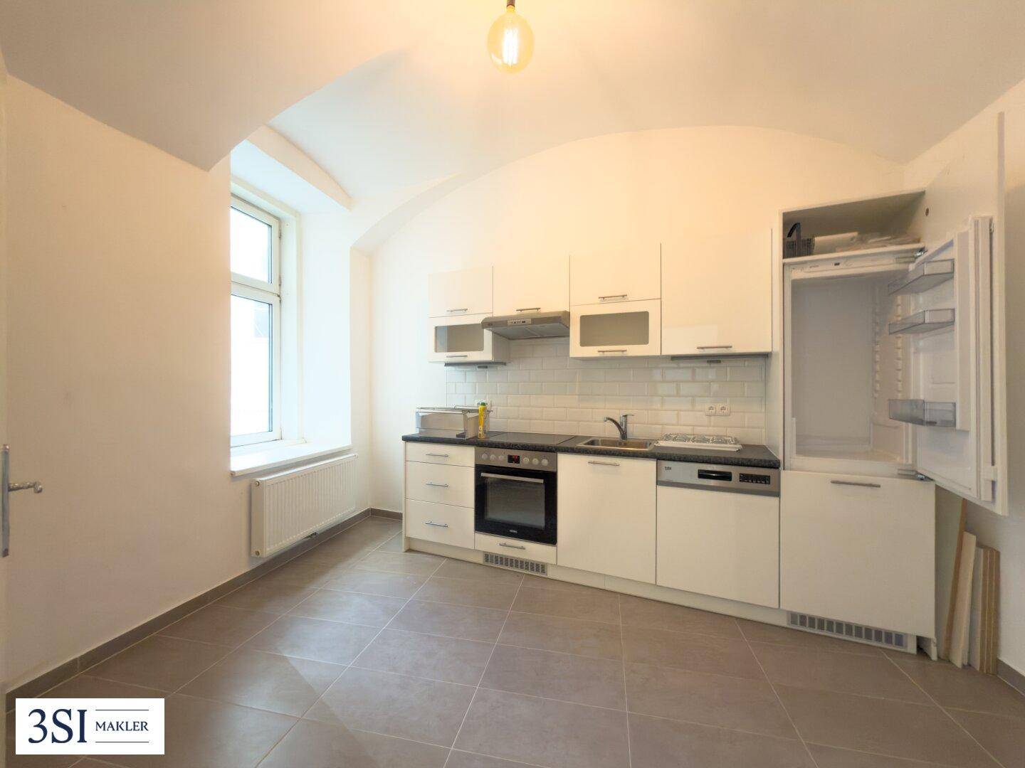Moderne Einbauküche mit weißen Schränken, schwarzen Arbeitsplatten und integrierten Geräten, hell und funktional.