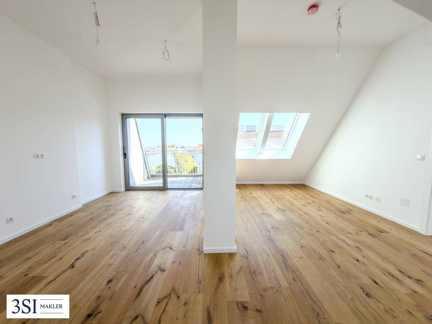 Heller, offener Raum mit Holzboden, Dachschrägen, großem Fenster und Zugang zu einem Balkon.