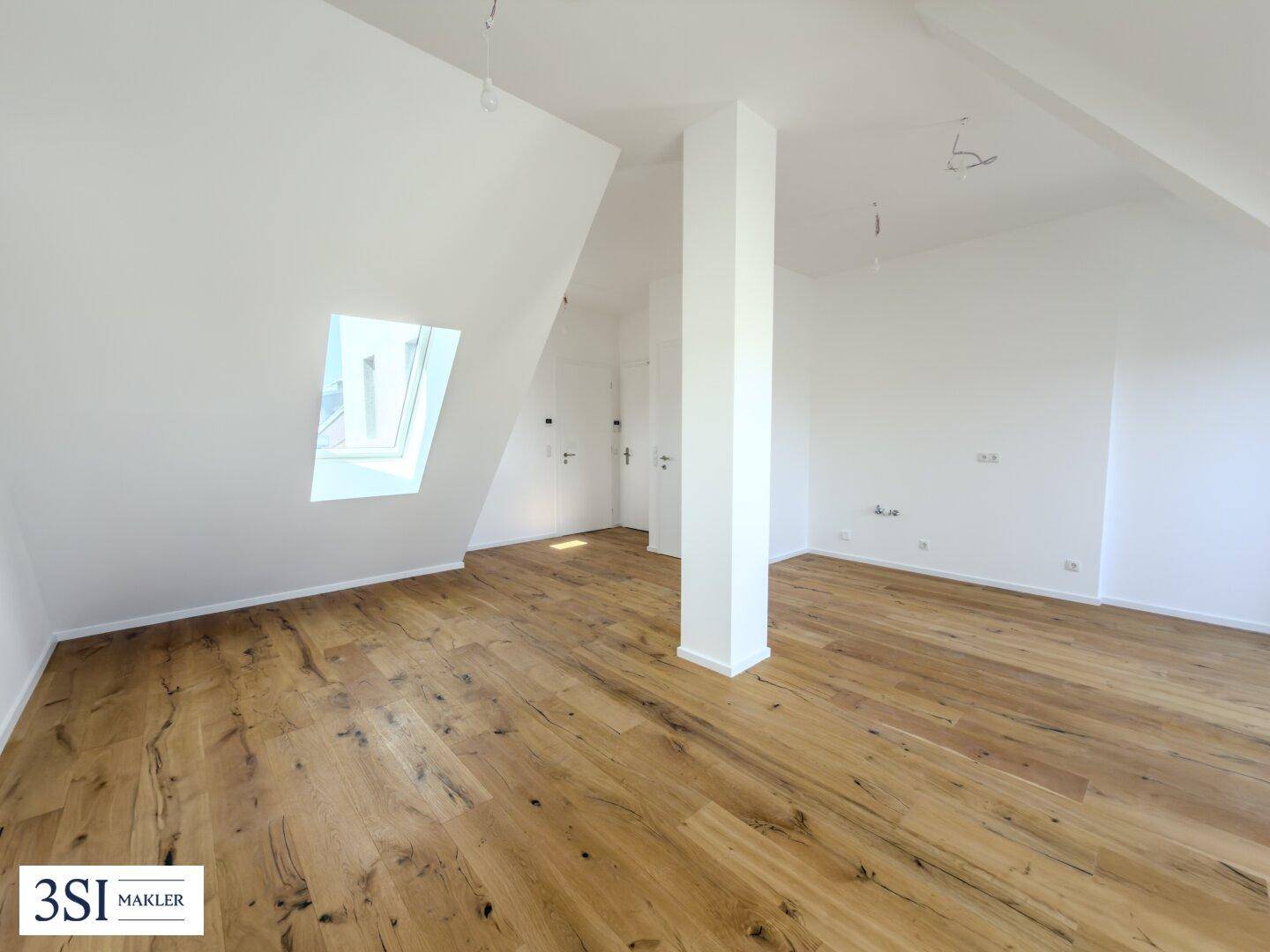 Heller Raum mit Holzboden, Dachschrägen und einem Oberlicht, der zu weiteren Zimmern führt.