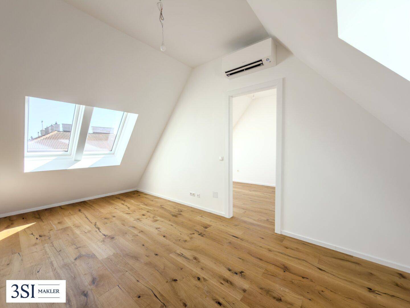 Helles Zimmer mit Holzboden, Dachschrägen, Dachfenster und installierter Klimaanlage.