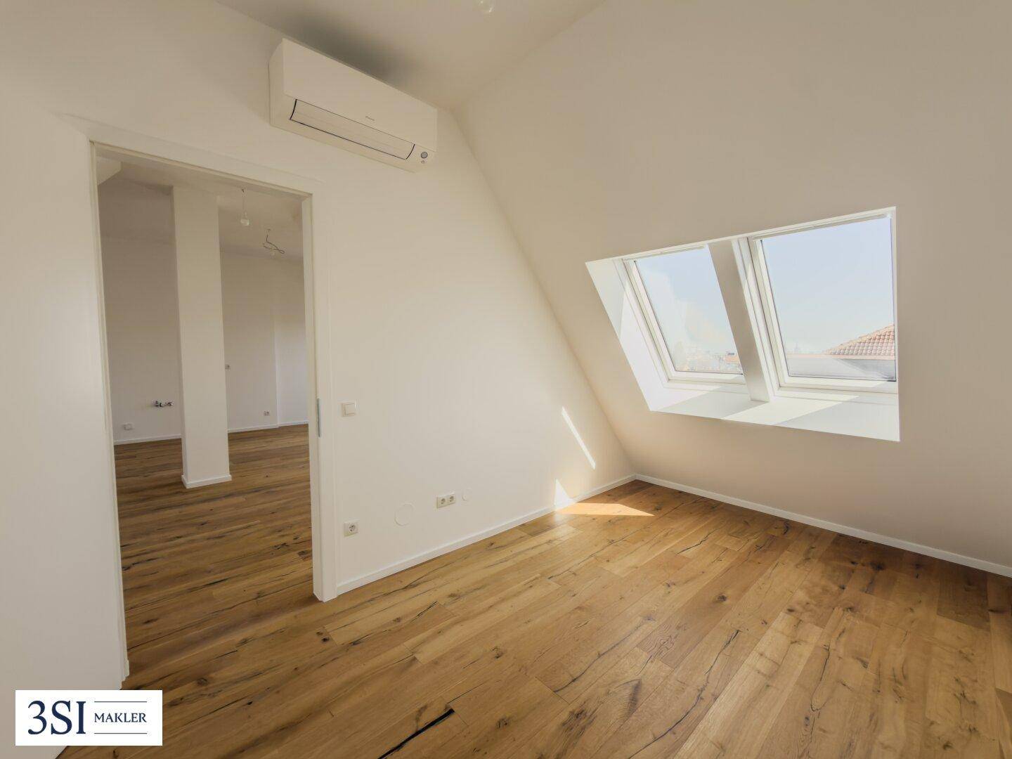 Helles Zimmer mit Holzboden, Dachschrägen, Dachfenstern und installierter Klimaanlage.