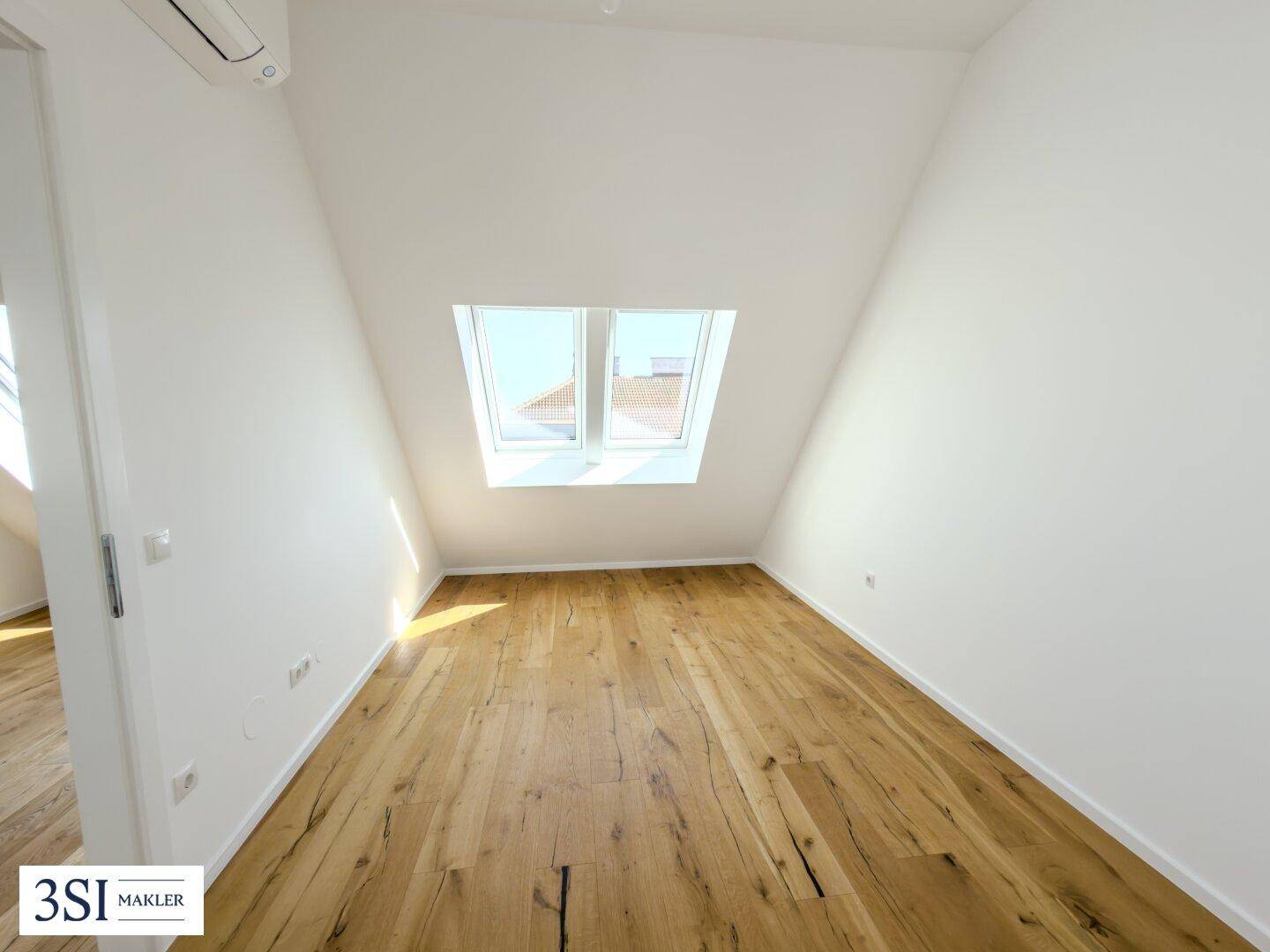 Geräumiges Zimmer mit Holzboden, Dachschrägen und zwei Dachfenstern für eine helle Atmosphäre.