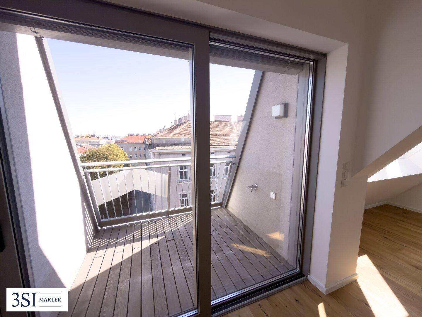 Moderner Balkon mit Holzboden, Metallgeländer und Blick über die Dächer der Stadt.