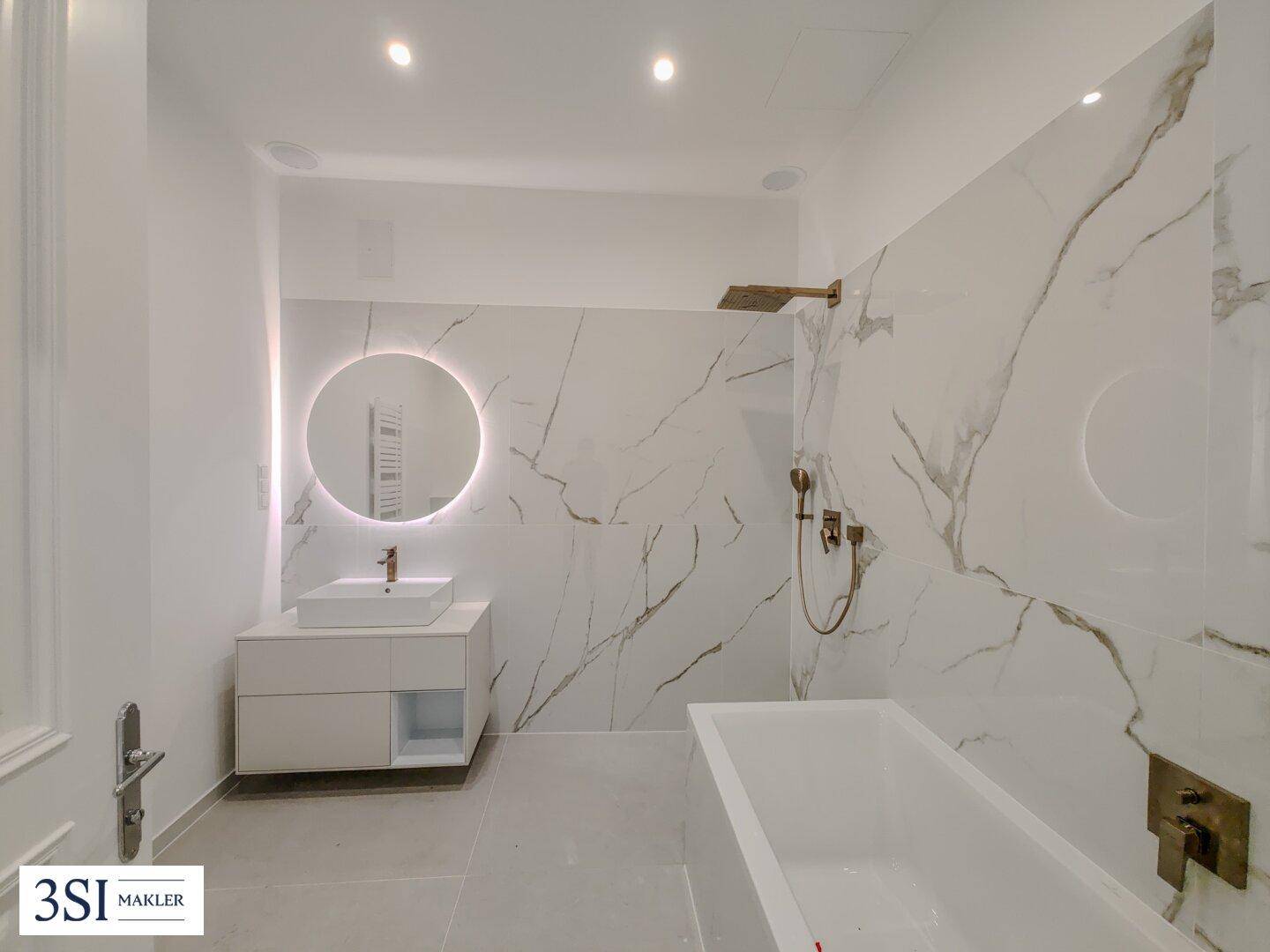 Modernes Badezimmer mit Badewanne, beleuchtetem Spiegel und eleganten Marmorfliesen, ausgestattet mit Regendusche.