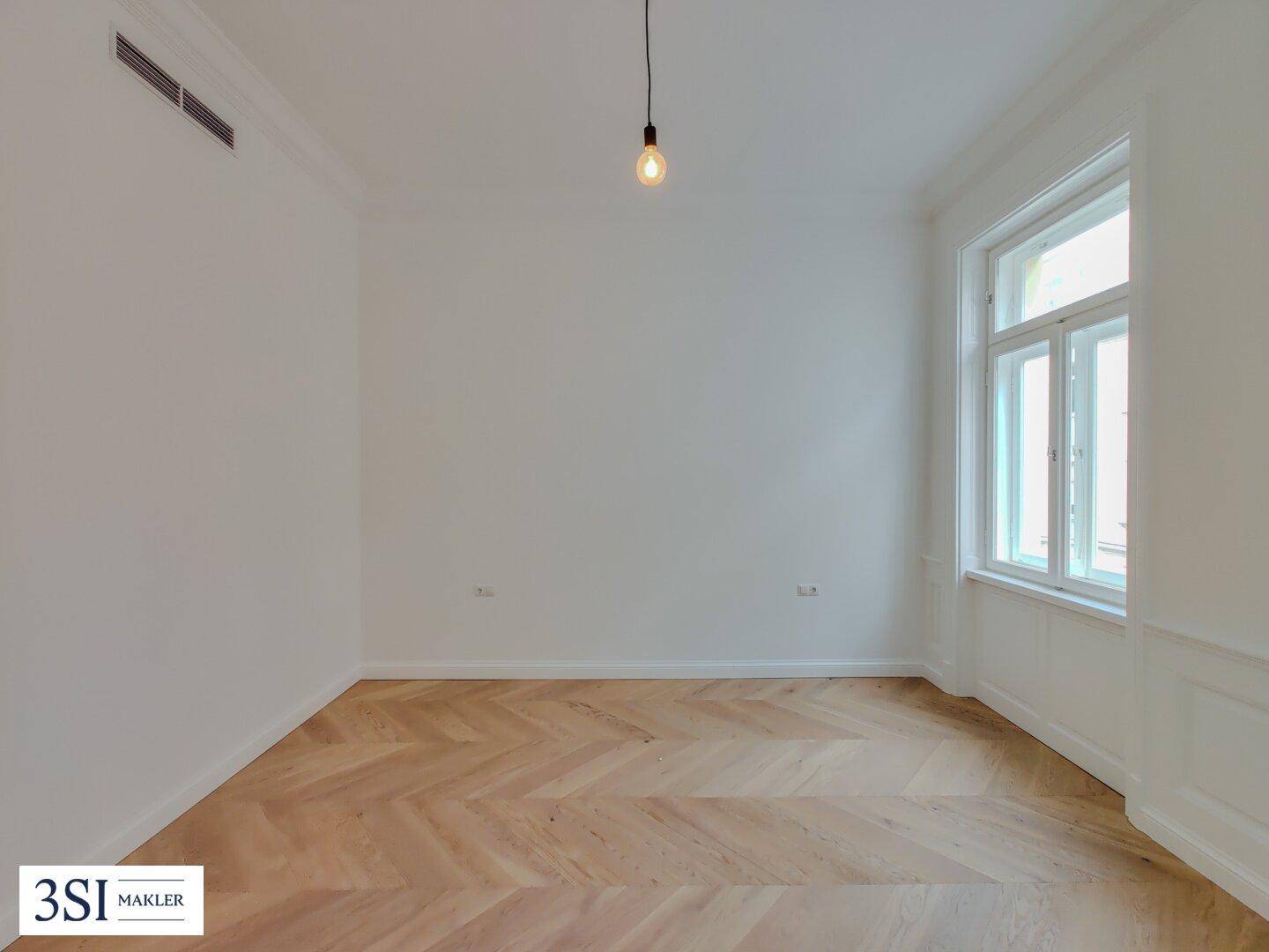 Ruhiges Zimmer mit Fischgrätparkett und großem Fenster, ideal als Schlaf- oder Arbeitszimmer nutzbar.
