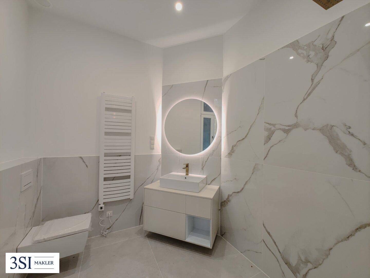 Modernes Badezimmer mit wandhängendem WC, beleuchtetem Spiegel und beheiztem Handtuchhalter, luxuriös ausgestattet.