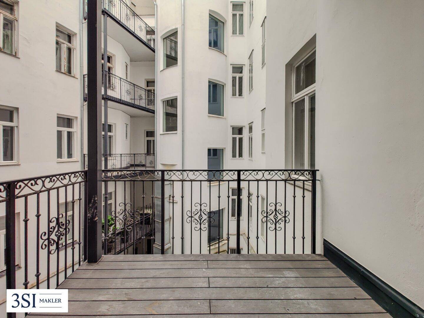 Balkon mit Holzboden und Blick auf den ruhigen Innenhof des Gebäudes, ideal zum Entspannen.