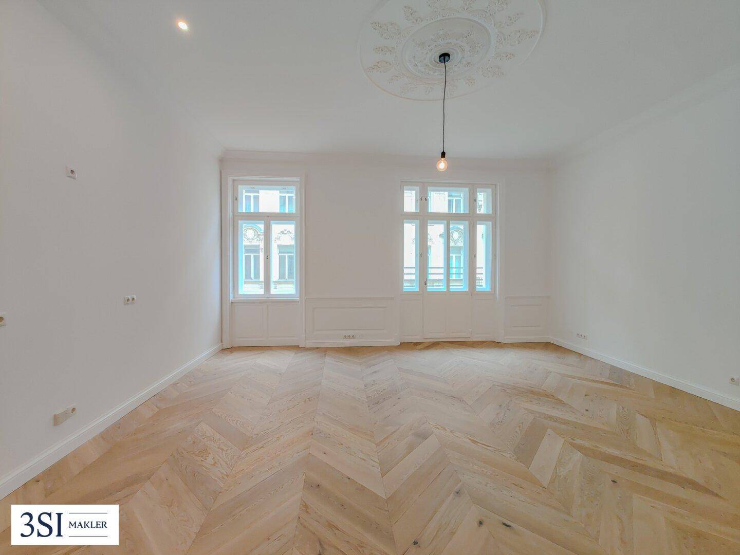 Großes Wohnzimmer mit Fischgrätparkett, Stuckdecke und hohen Fenstern für viel Licht und Eleganz.