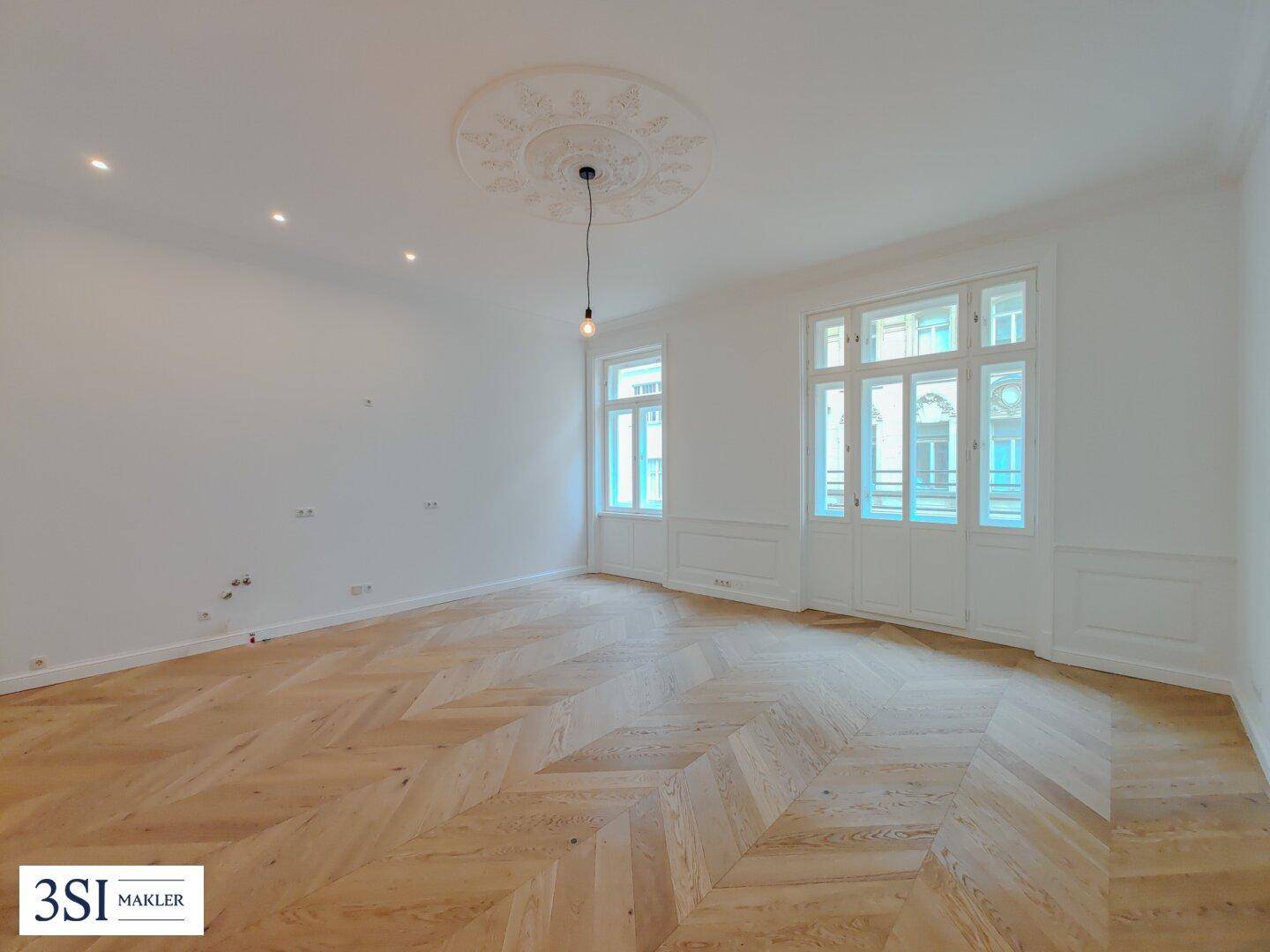 Helles Zimmer mit Fischgrätparkett, hohen Decken und dekorativem Deckenmedaillon, frisch renoviert.