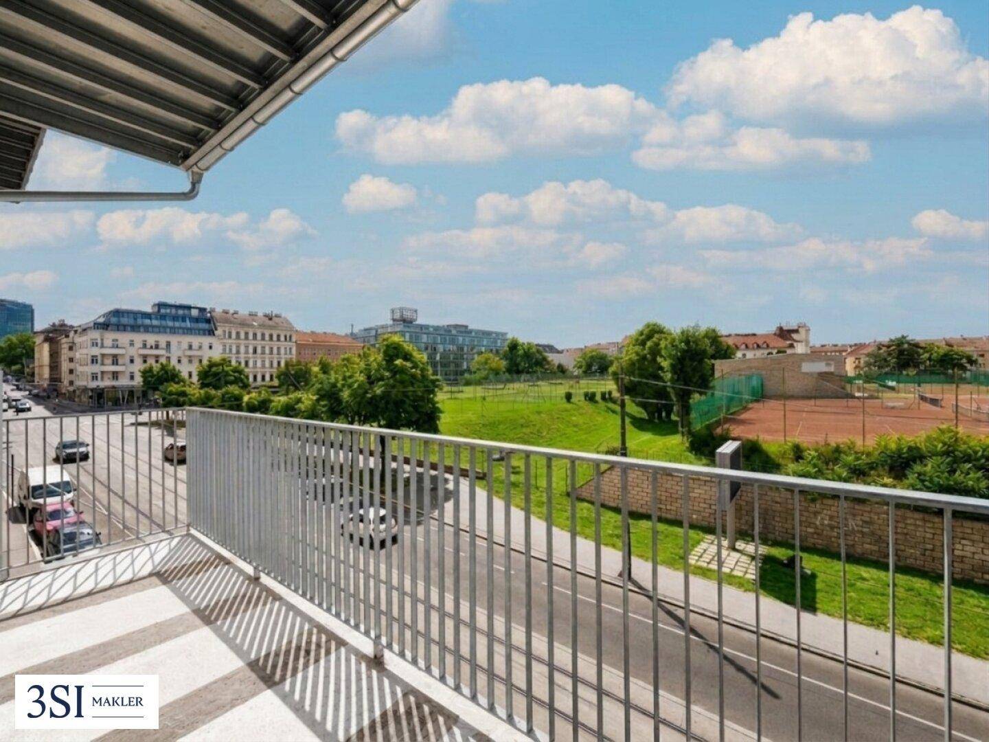 Balkon mit Blick auf die Stadt, Grünflächen und einen Tennisplatz.