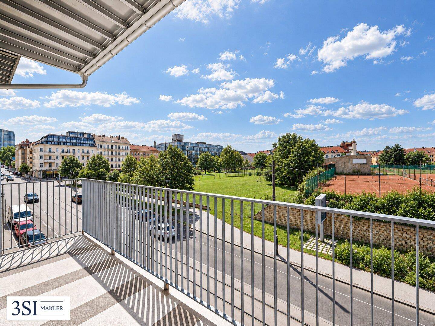 Balkon mit Blick auf eine Grünfläche, Tennisplätze und die umliegende Stadtbebauung.
