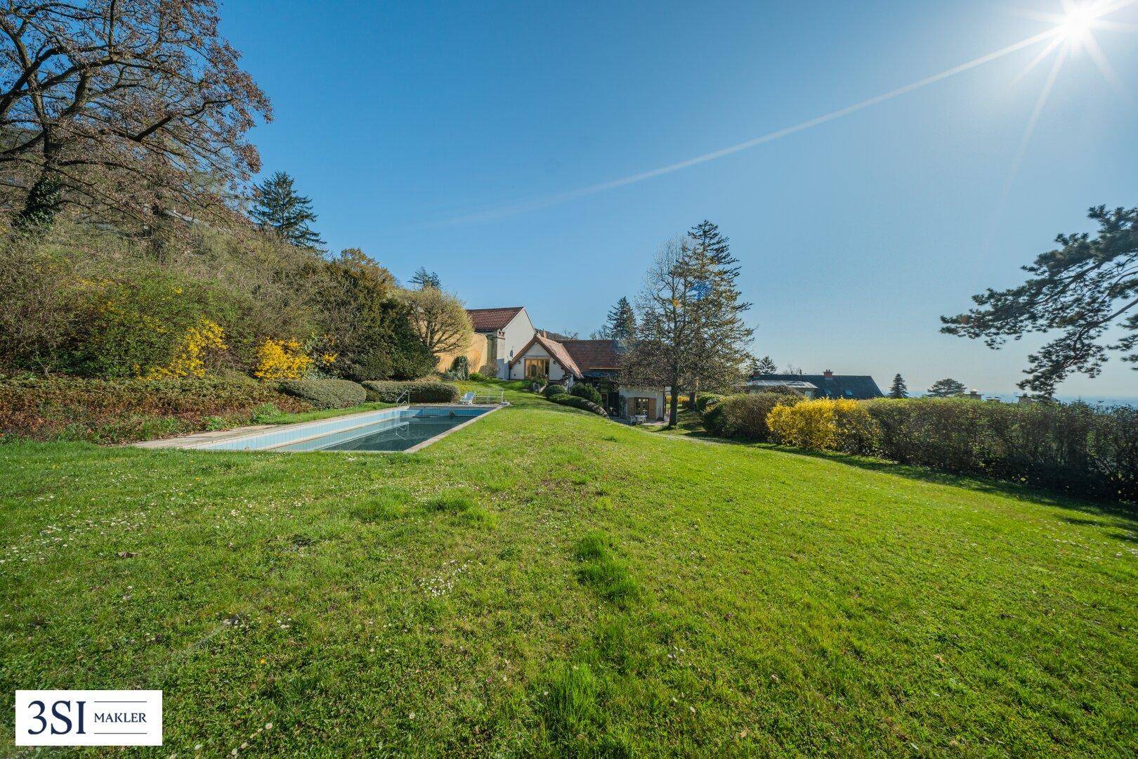 Weitläufiger Garten mit Rasenfläche, Pool und Blick auf das Anwesen unter strahlend blauem Himmel.