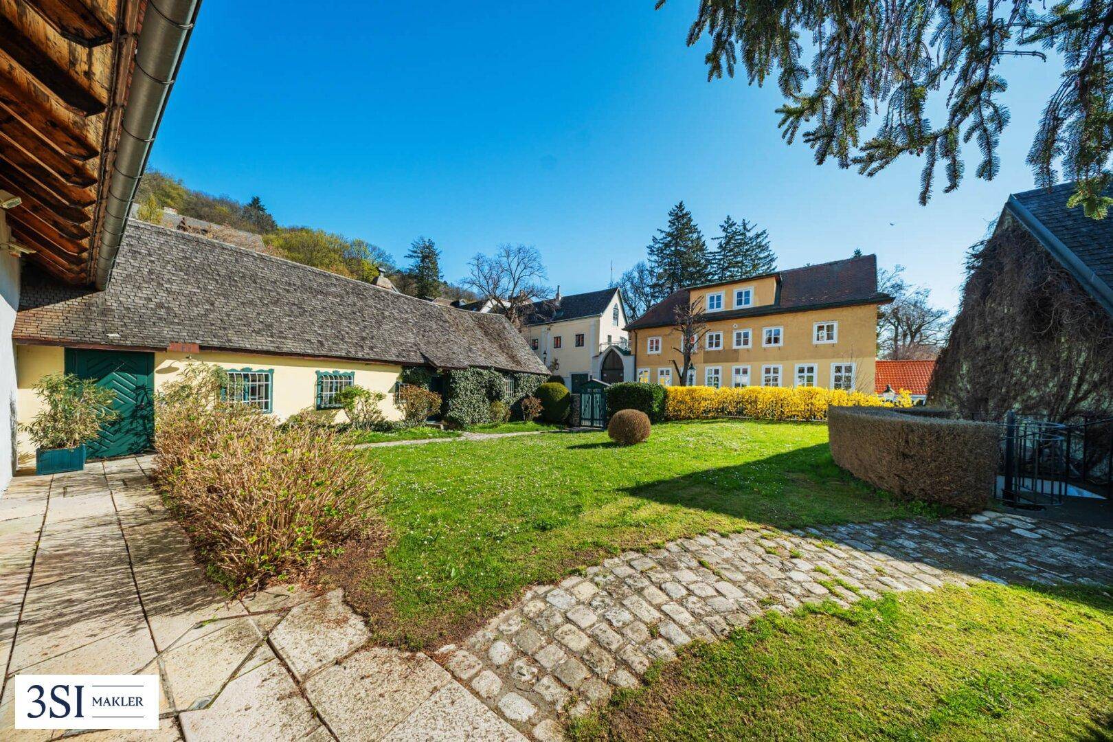 Idyllischer Innenhof mit Rasenfläche, gepflasterten Wegen und historischen Gebäuden.