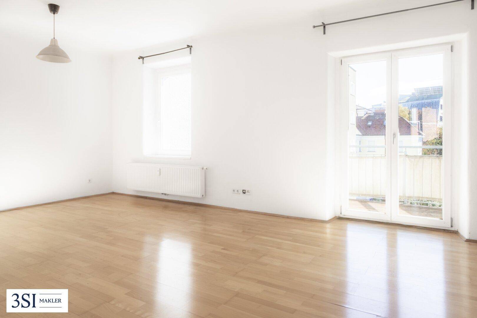 Heller Wohnraum mit hellem Parkettboden, weißen Wänden und Zugang zu einem Balkon.