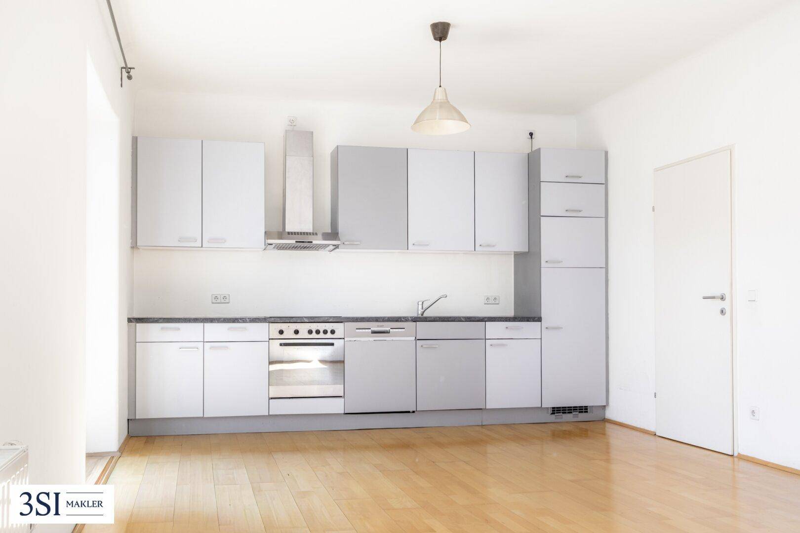 Moderne Einbauküche mit hellgrauen Schränken, Holzfußboden und integrierten Geräten.