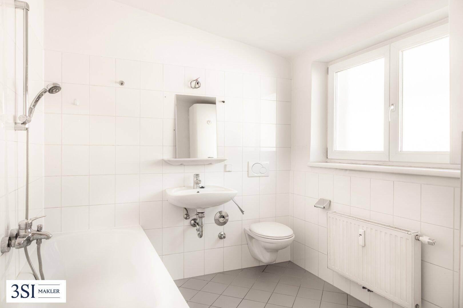 Helles Badezimmer mit weißen Fliesen, Badewanne mit Duschfunktion und Fenster.
