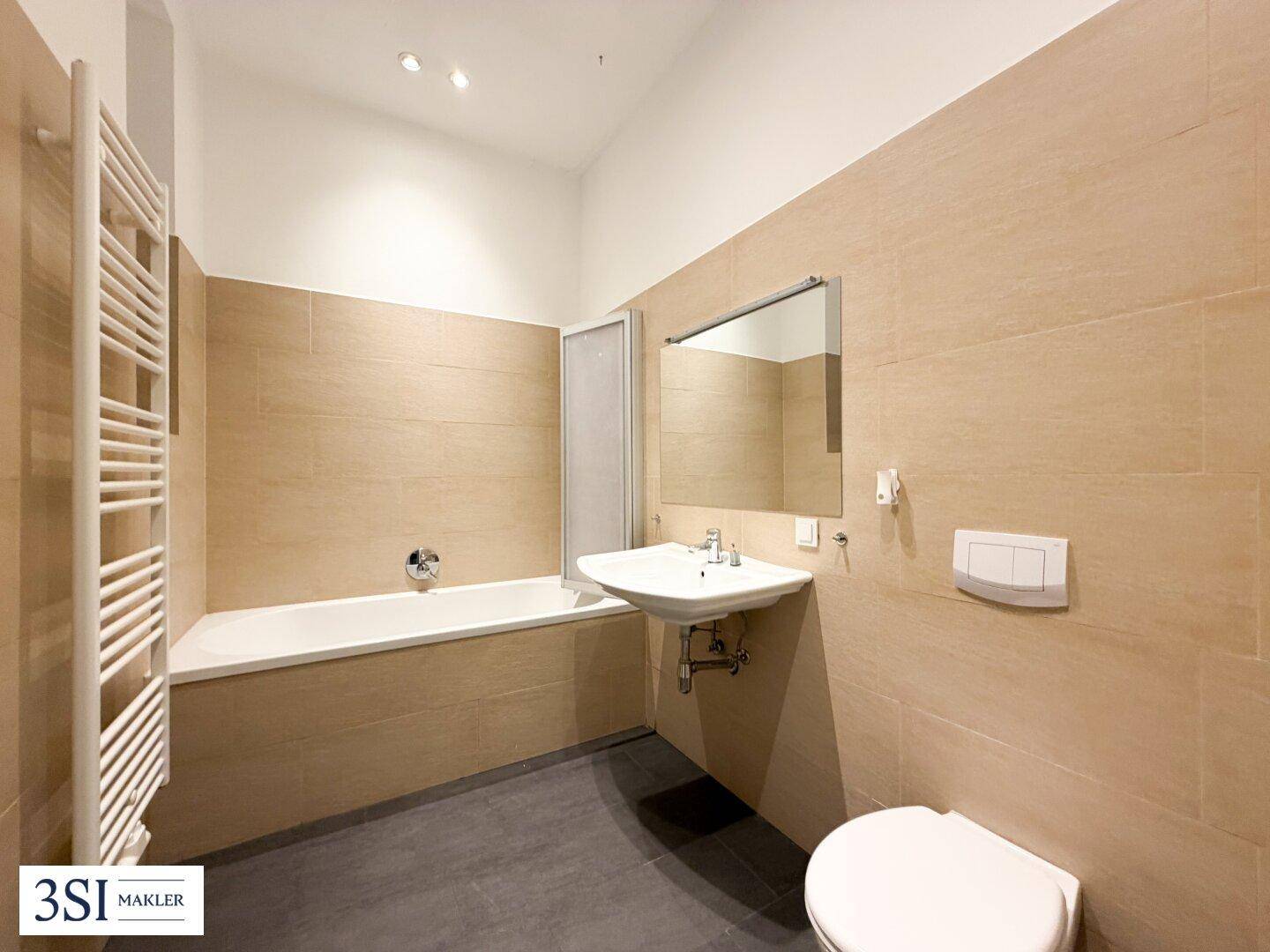 Modernes Badezimmer mit Badewanne, WC, Waschbecken und beigen Fliesen.