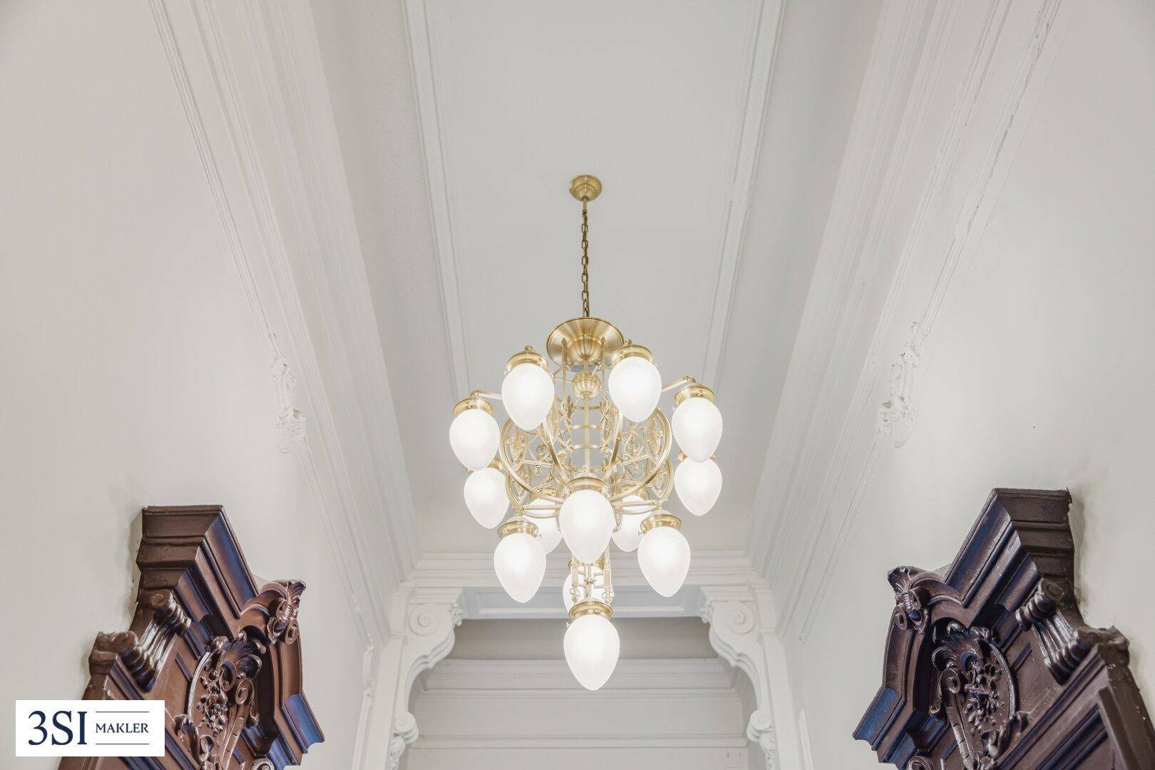 Prunkvoller Kronleuchter und verzierte Decke in einem eleganten Flur.