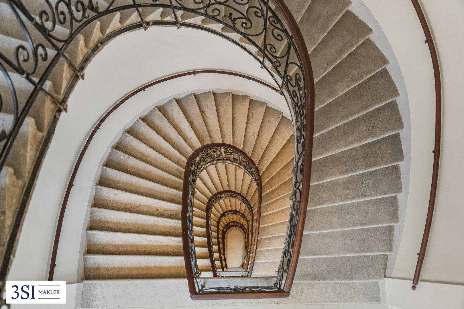 Elegante Wendeltreppe mit Steinstufen und schmiedeeisernem Geländer von oben betrachtet.