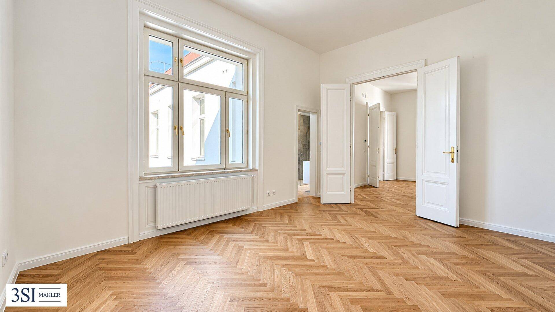 Geräumiges Zimmer mit Fischgrätparkett, hohen Decken und großen Fenstern.