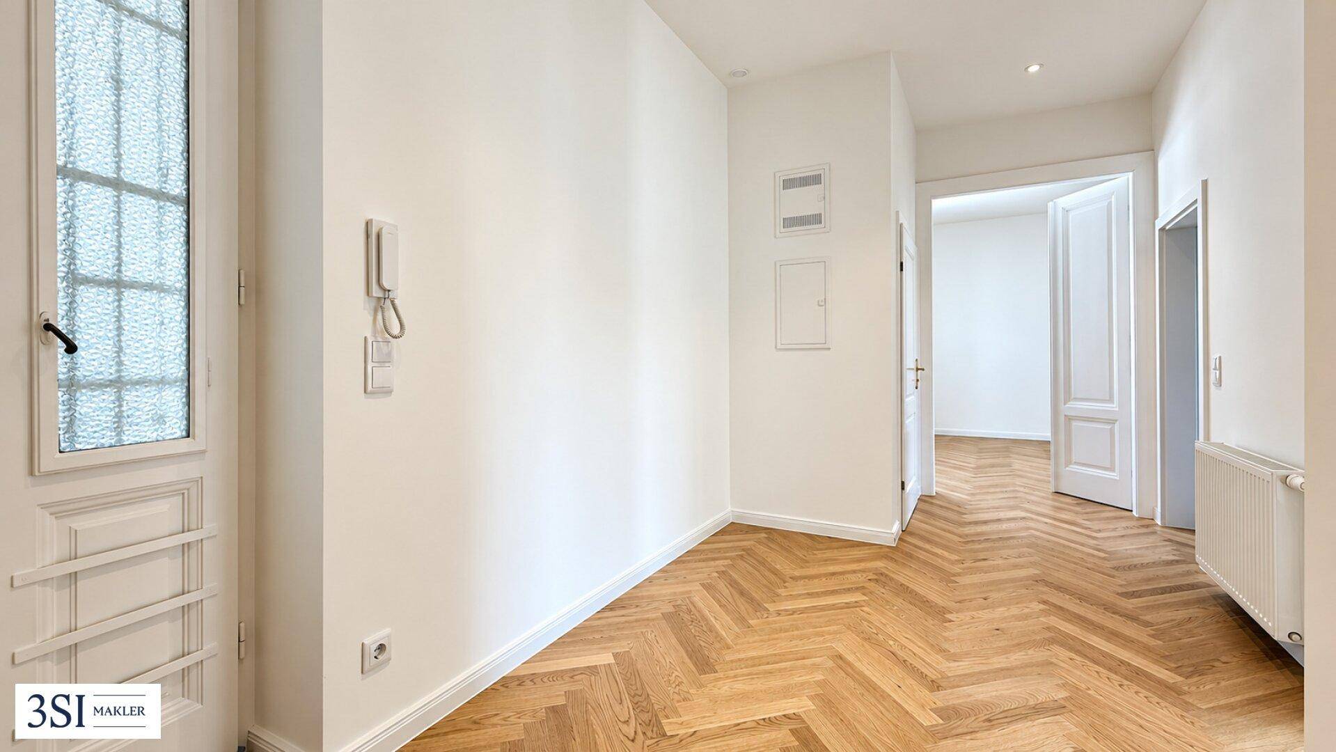 Heller Flur mit Fischgrätparkett und Gegensprechanlage, der zu weiteren Räumen führt.