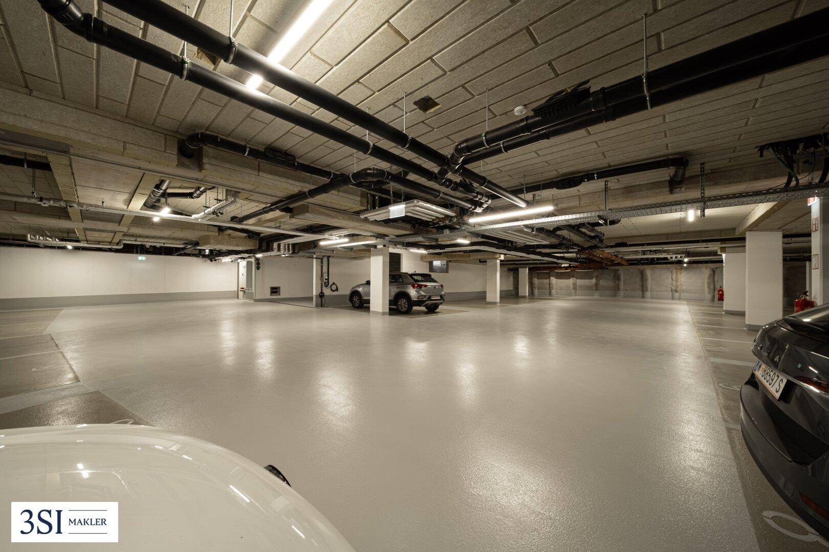 Geräumige Tiefgarage mit ausreichend Stellplätzen und sichtbaren Installationen an der Decke.