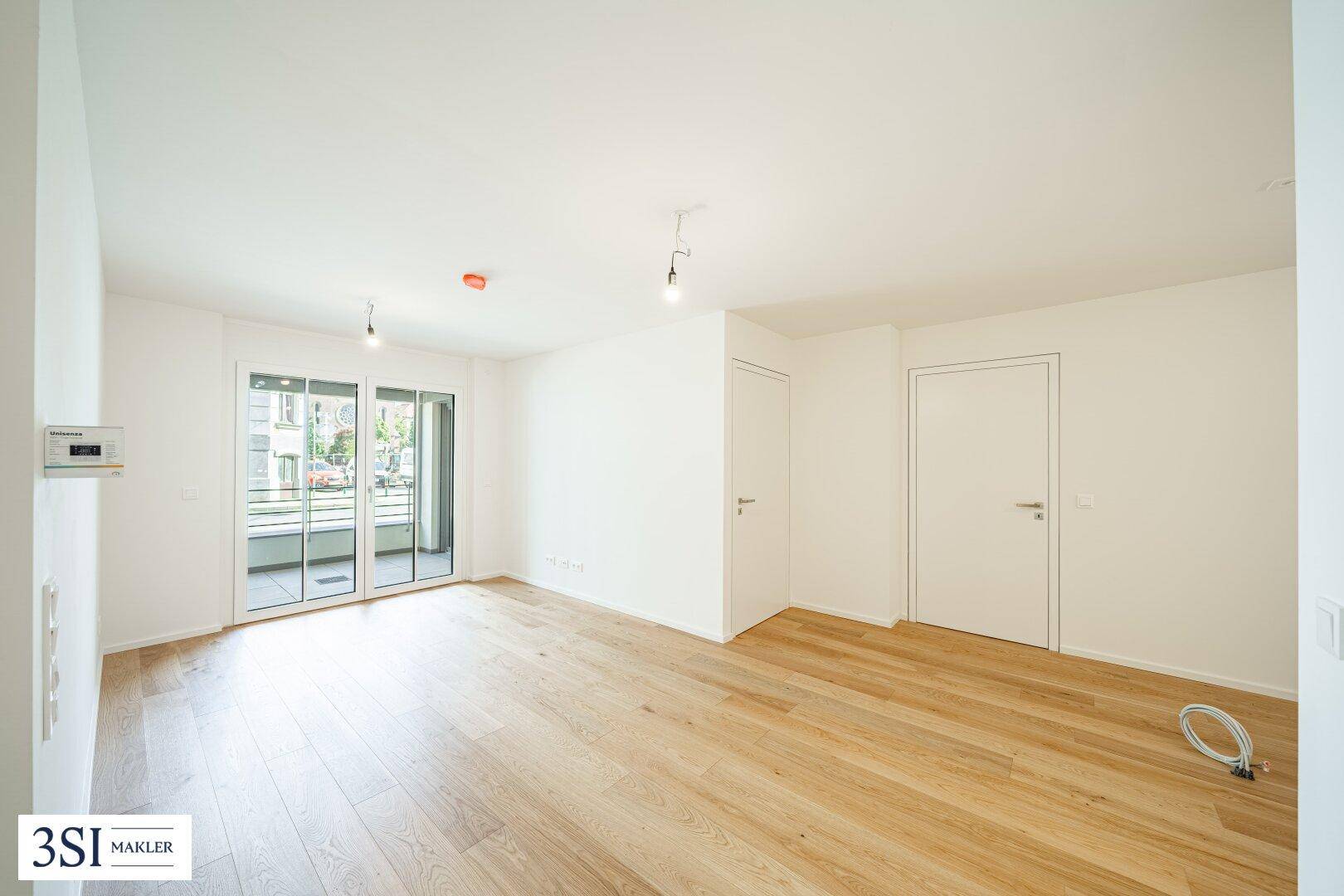 Helles Wohnzimmer mit Holzboden und Zugang zu einem Balkon, bereit für die individuelle Einrichtung.