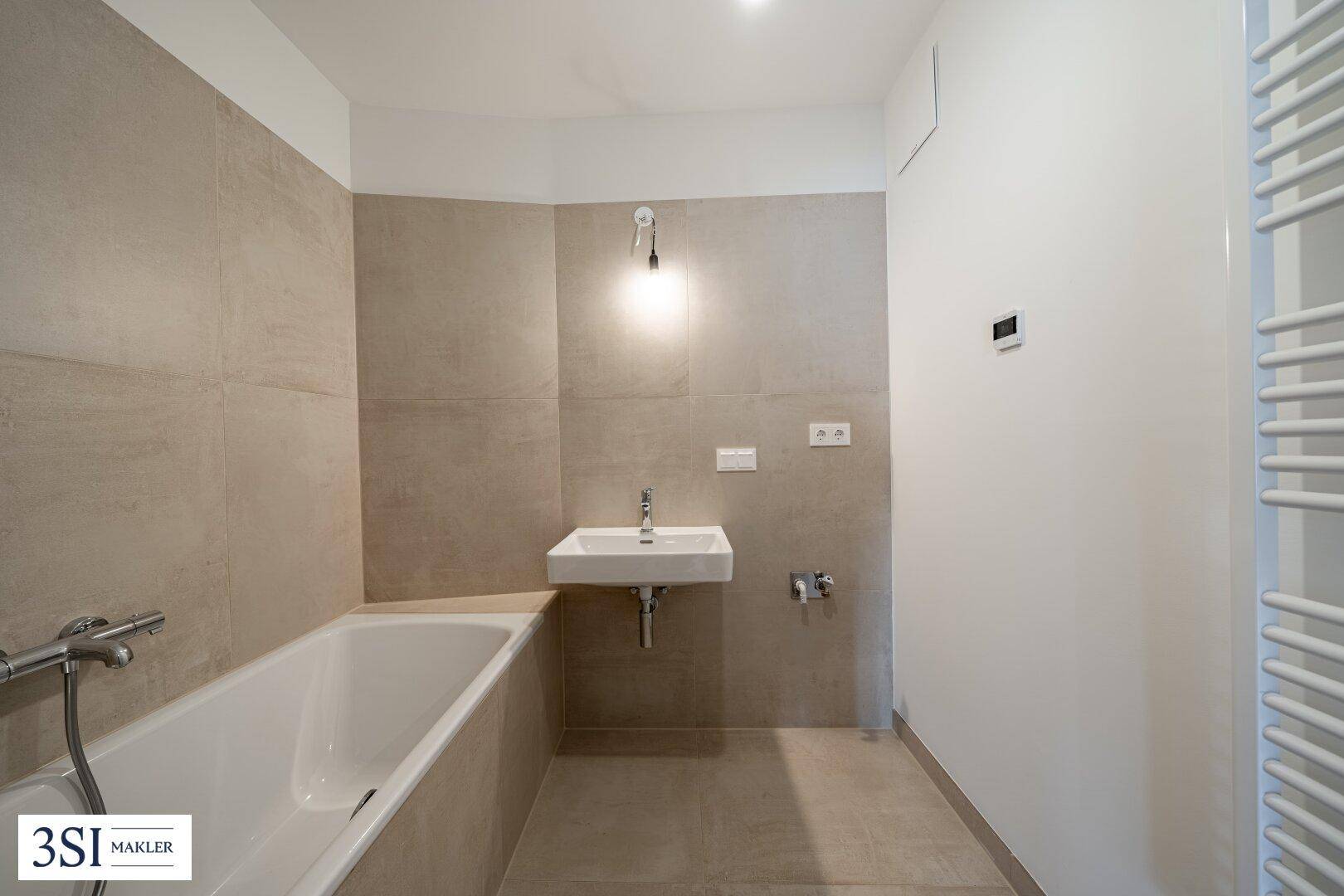 Modernes Badezimmer mit Badewanne, Einzelwaschbecken und beheiztem Handtuchhalter an der Wand.