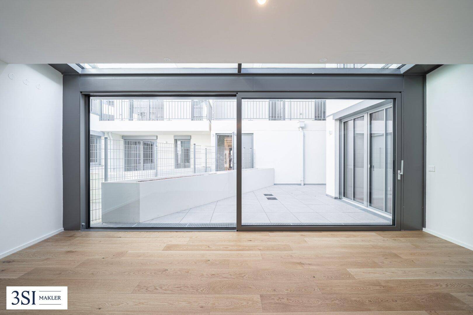 Heller Wohnraum mit großen Schiebetüren, die zu einer privaten Terrasse im Innenhof führen.
