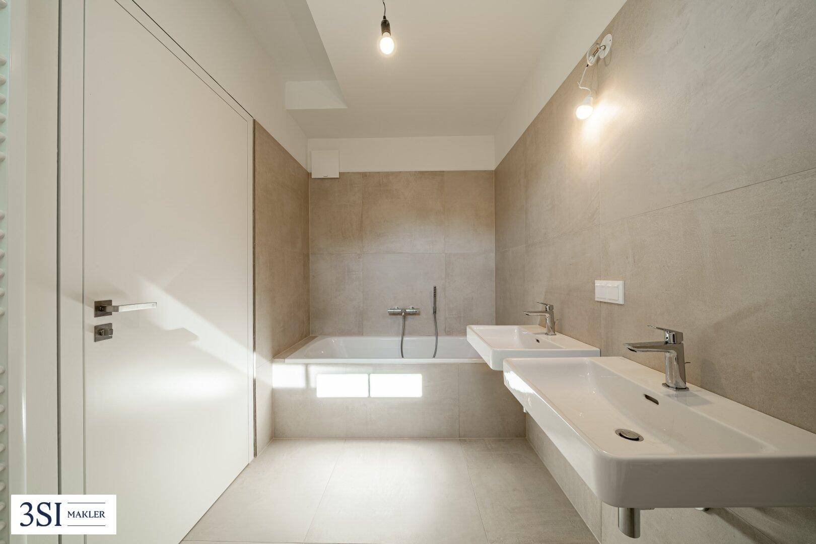 Modernes Badezimmer mit zwei Waschbecken, Badewanne und hellen Fliesen an den Wänden.