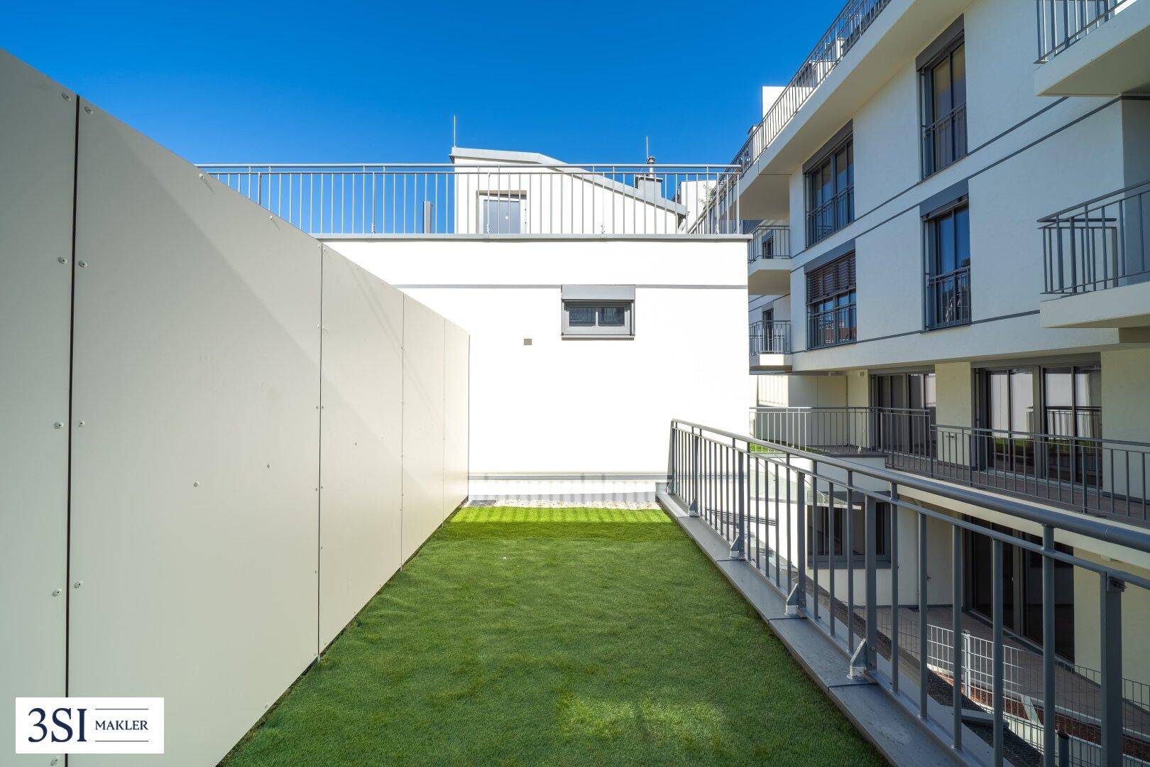 Private Dachterrasse mit Kunstrasen und Blick auf die umliegenden Gebäude unter blauem Himmel.