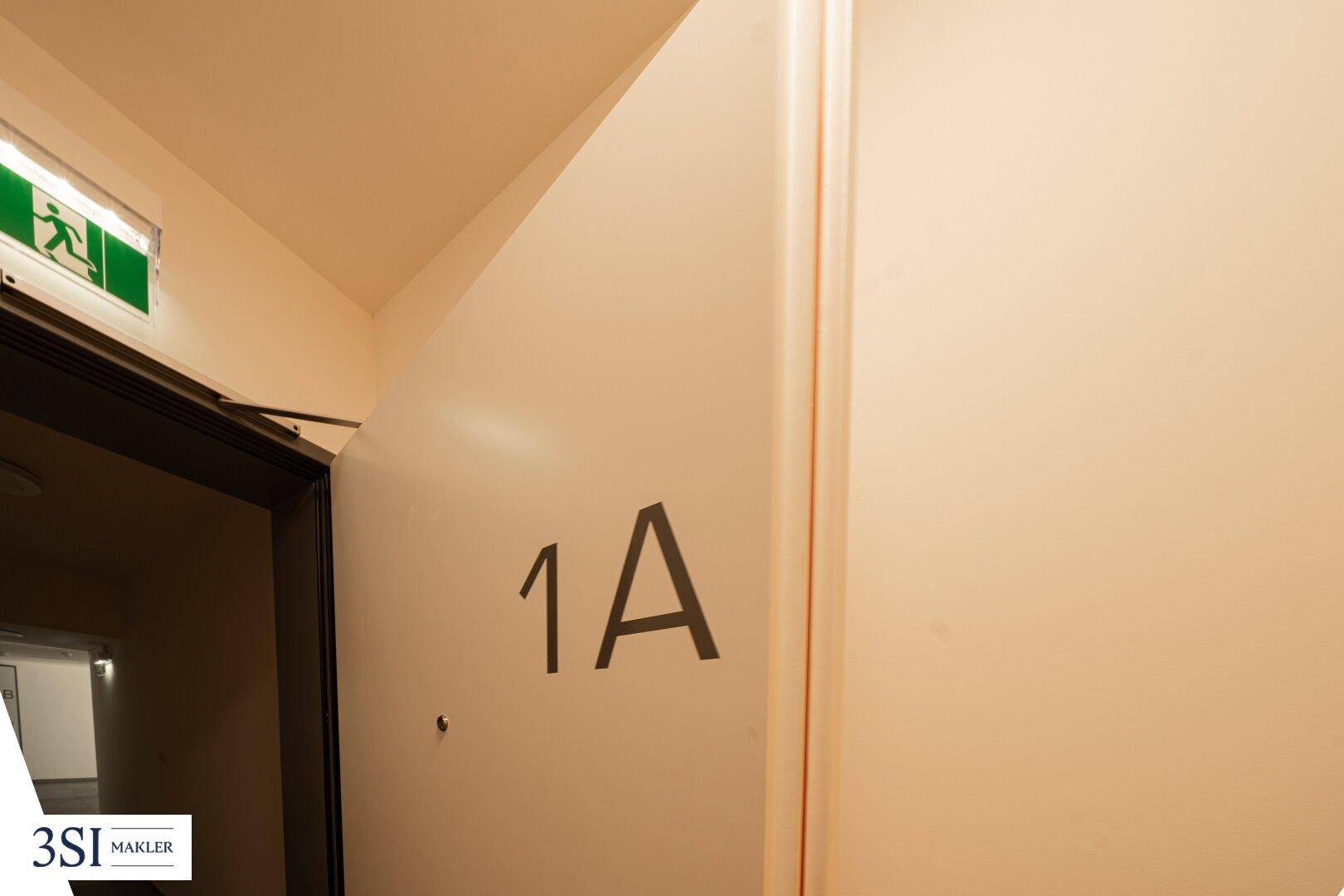 Eingangsbereich einer Wohnung mit Türbeschriftung "1A" und Notausgangsschild.