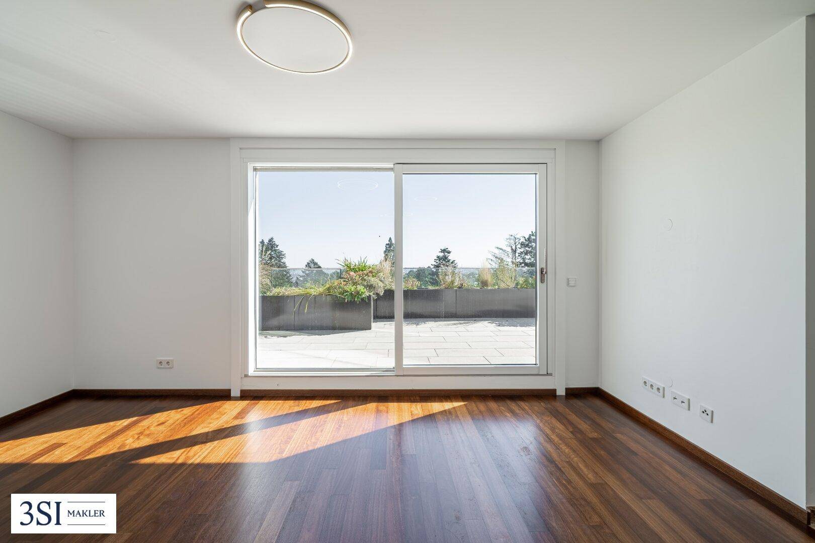 Heller Raum mit großen Schiebetüren, die auf eine Terrasse führen, und dunklem Holzparkettboden.