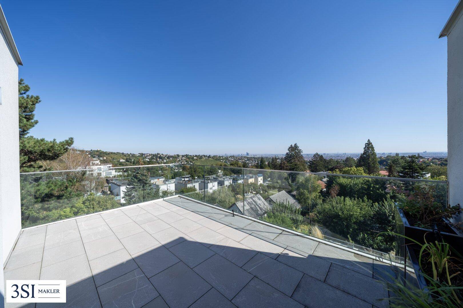 Weitläufige, unmöblierte Terrasse mit Glasgeländer und Panoramablick über die Stadt und die grüne Umgebung.