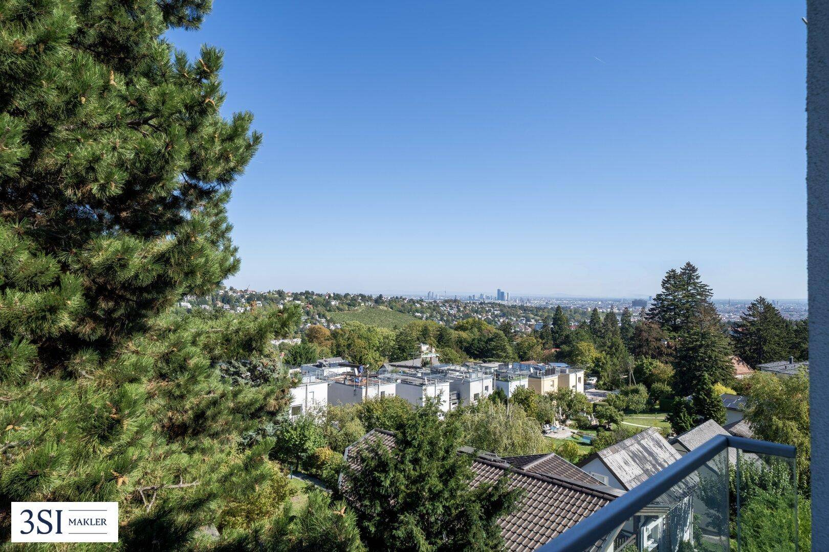Malerischer Ausblick auf die Stadt und die umliegende grüne Natur, umrahmt von hohen Bäumen.