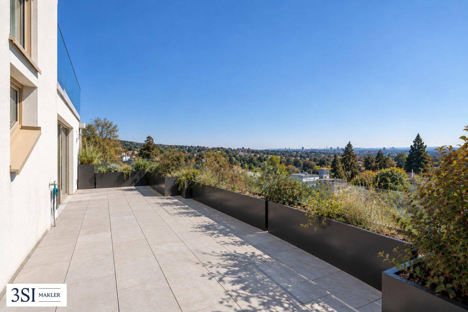 Weitläufige Terrasse mit großen Pflanzgefäßen und Panoramablick über die grüne Landschaft und die Stadt.