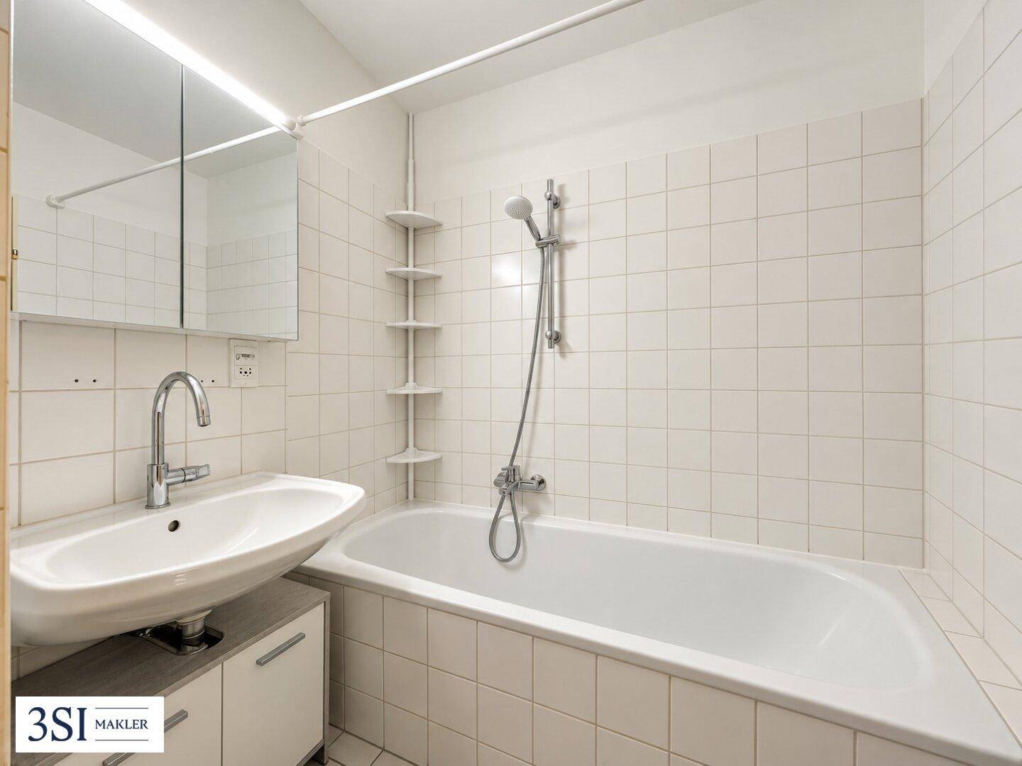 Funktionales Badezimmer mit Badewanne, Waschbecken, Spiegelschrank und weißen Wandfliesen.
