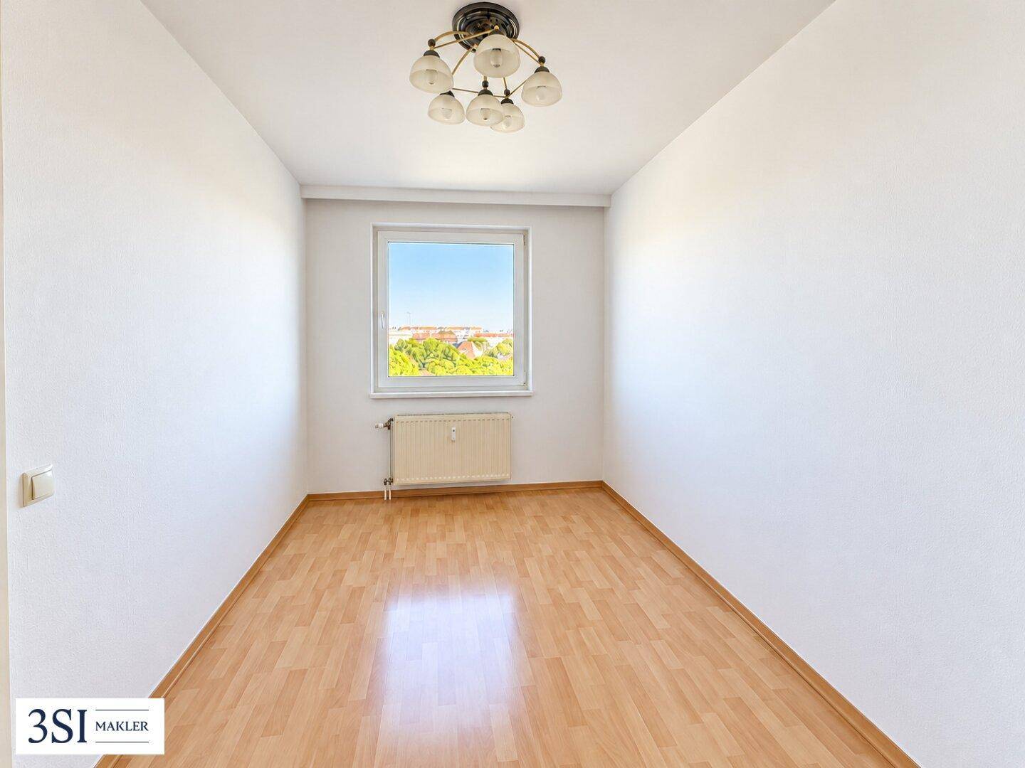 Helles Schlafzimmer mit Parkettboden, weiß gestrichenen Wänden und einem Fenster mit Ausblick ins Grüne.